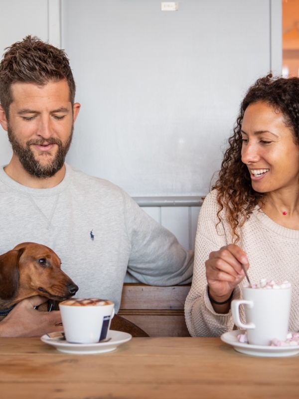 a man, woman and a dog sitting at a table with coffee cups in front of them